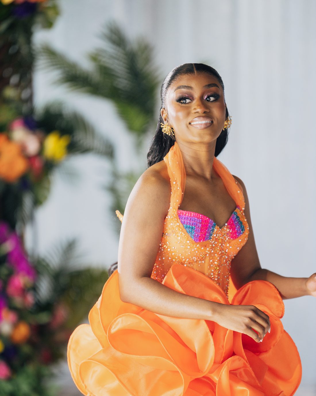 A bride in an orange gown photographed among tropical florals